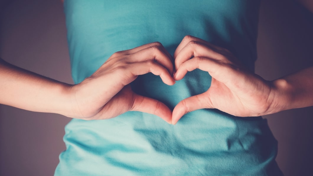 Person holding their hands to form a heart shape in front of their stomach indicating good gut health