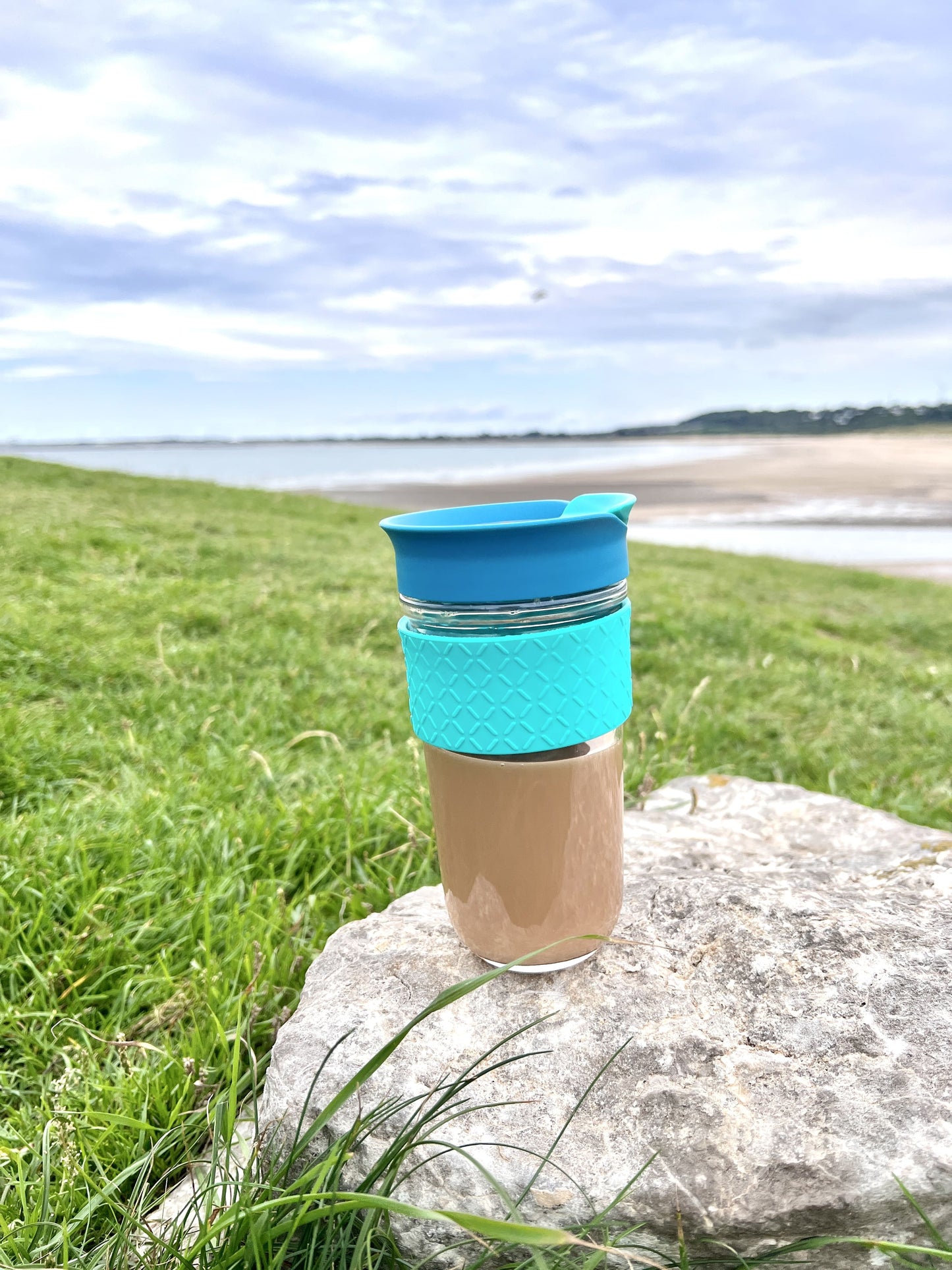 SoleCup glass travel mug containing tea placed on a rock by the beach